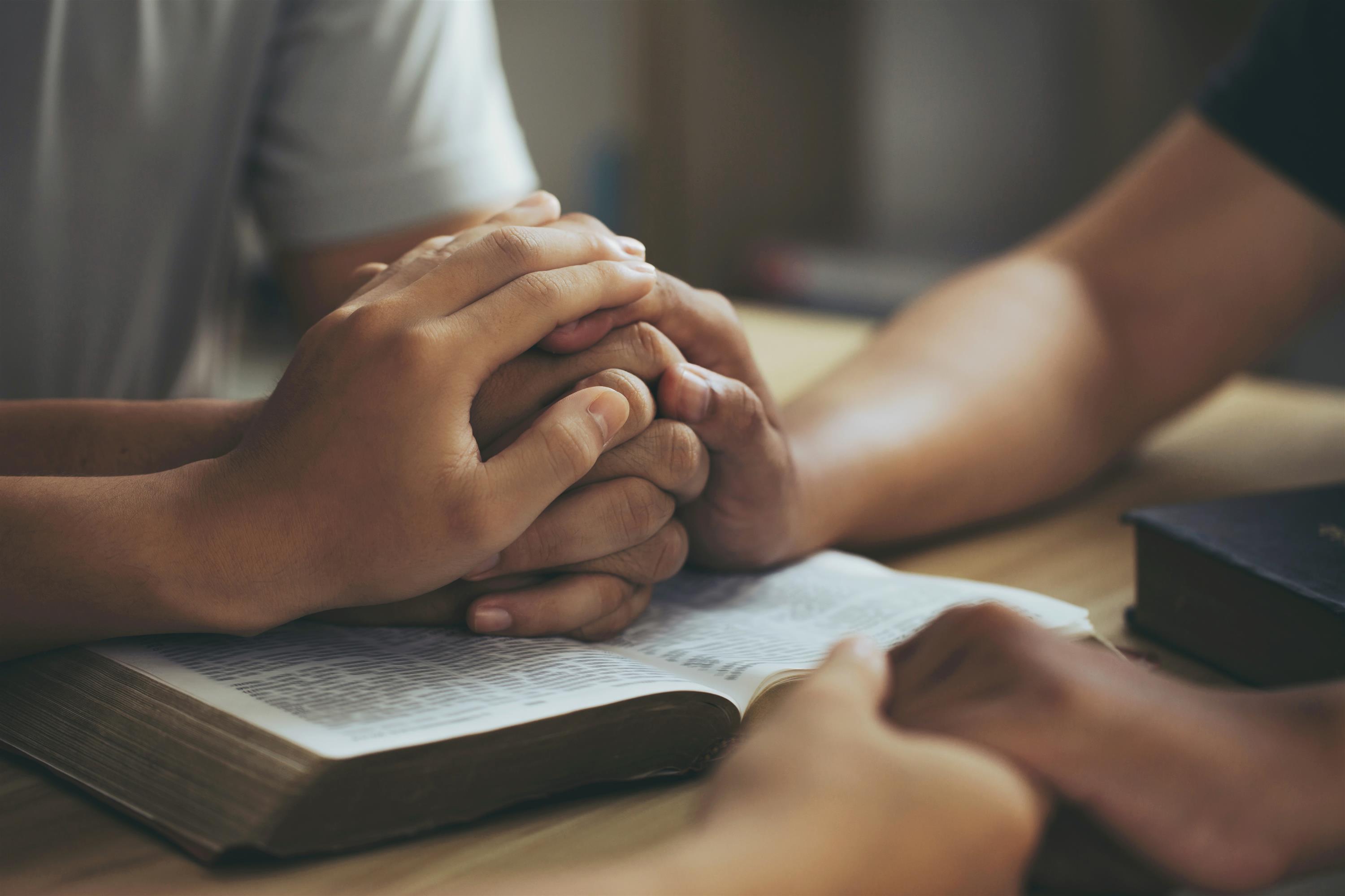 People holding hands over a Bible